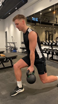 a man squatting with a kettlebell in a gym